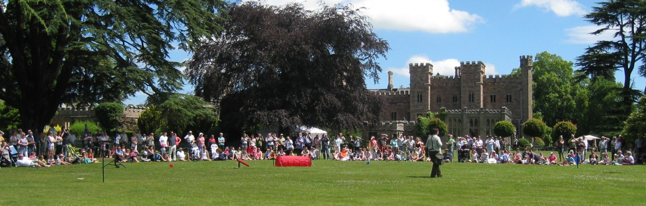 A crowd of people sitting on the grass in front of Hampton Court Castle